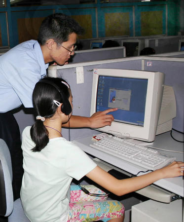 網(wǎng)絡知識伴成長 工作人員熱心輔導來上網(wǎng)的小學生